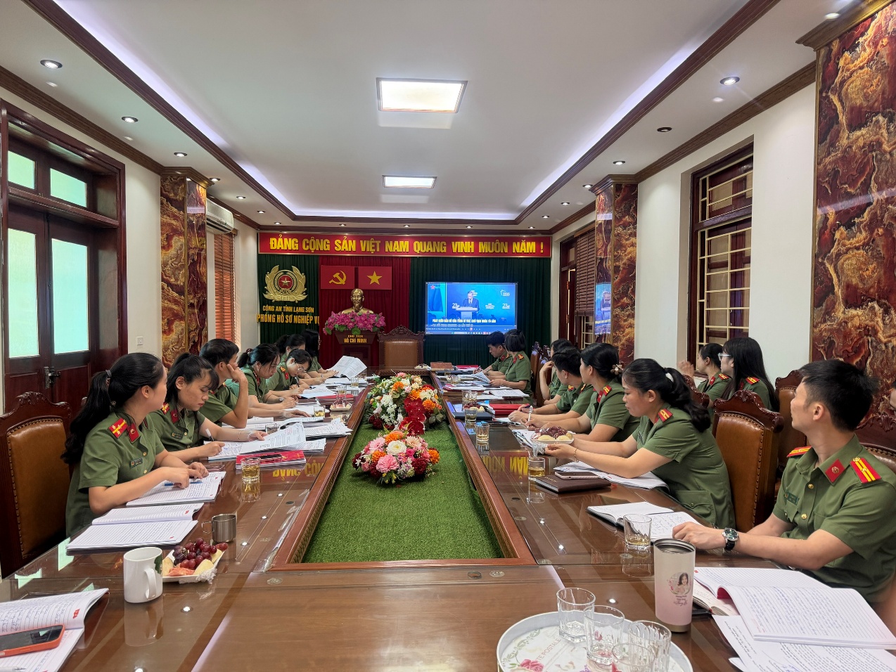 The image shows a group of people in military uniforms seated around a long table in a room with decorative elements and a presentation screen.

AI-generated content may be incorrect.